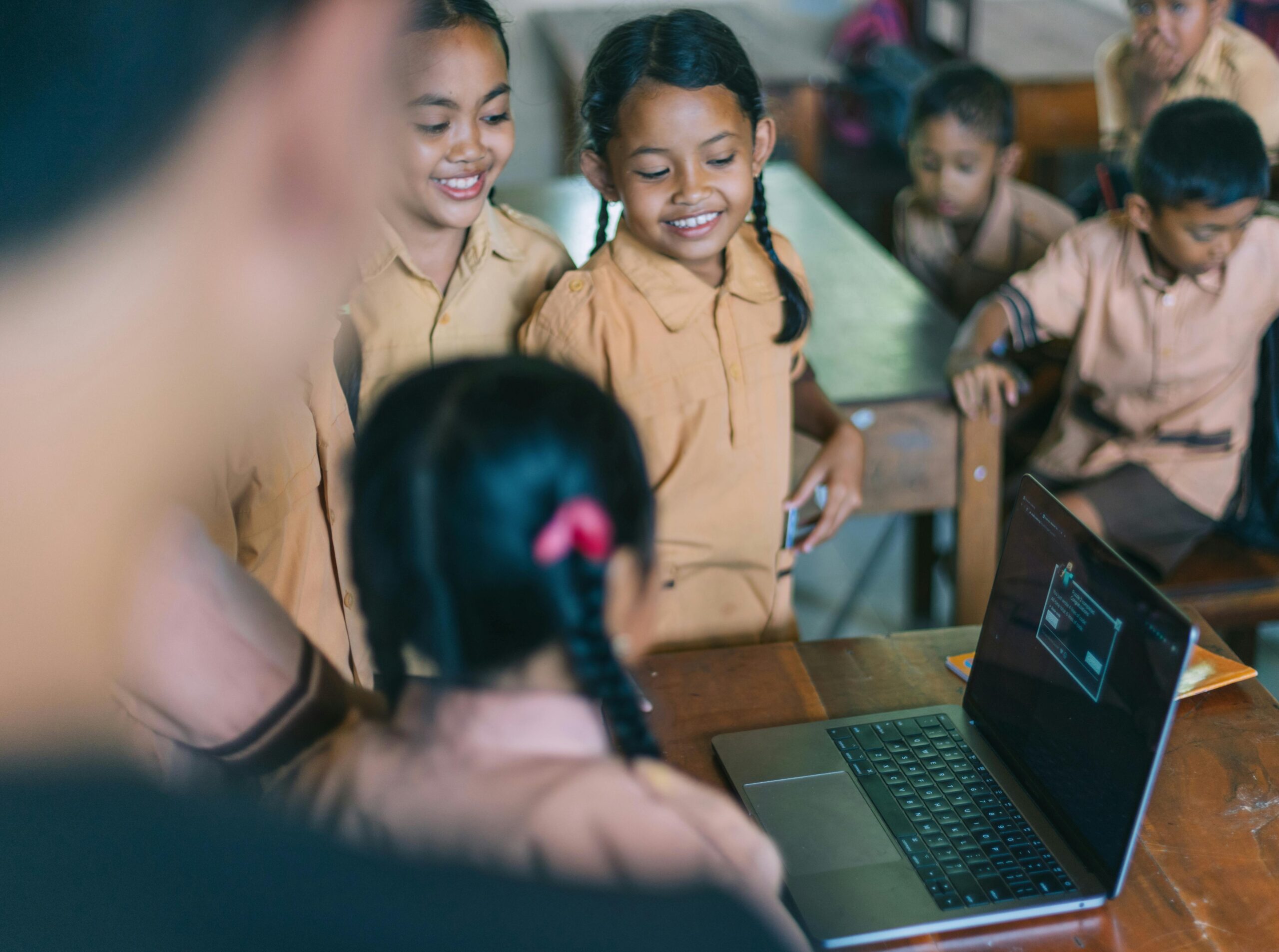 Smiling children engaged in a group learning activity with a laptop in a classroom setting.